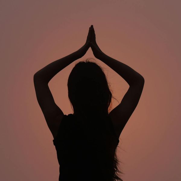 Woman in a calm yoga pose in a dark room with sunset light.